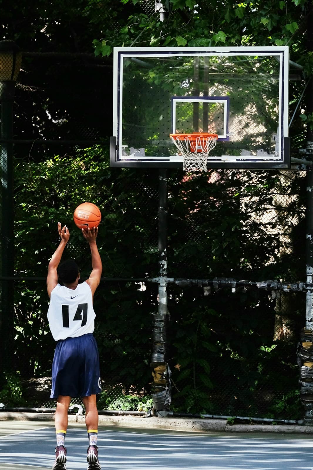 A player seen from behind shooting at a full-height outdoor hoop