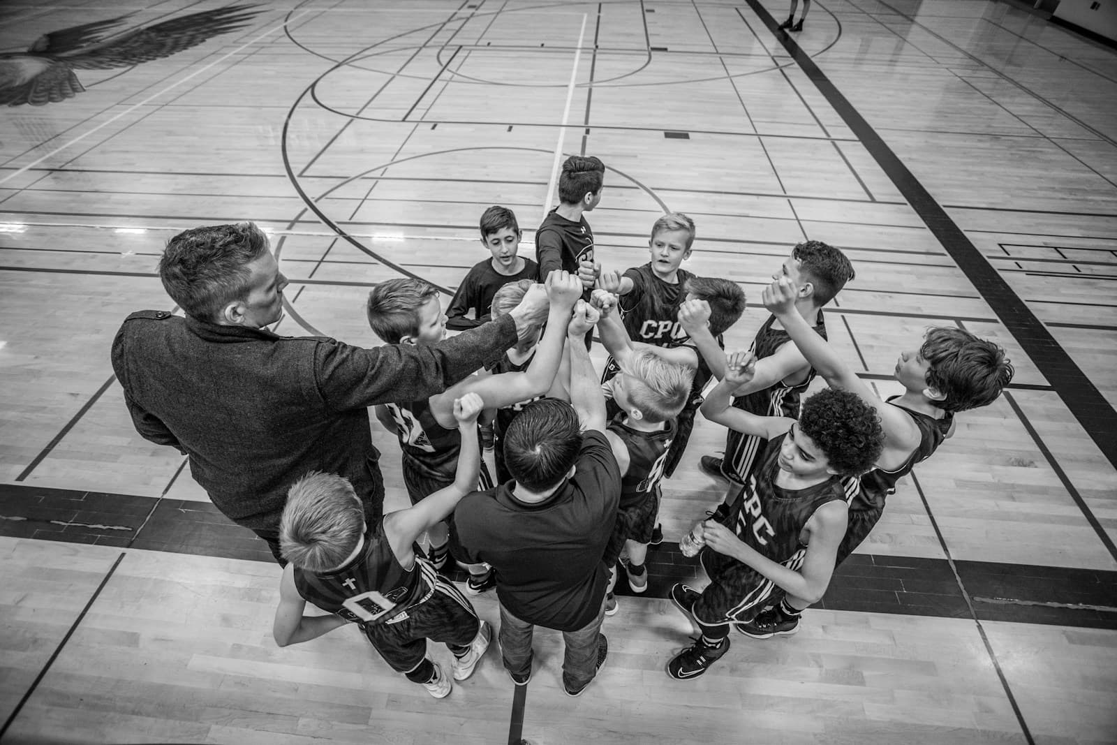A youth team and their coach huddled with hands together on a gym floor