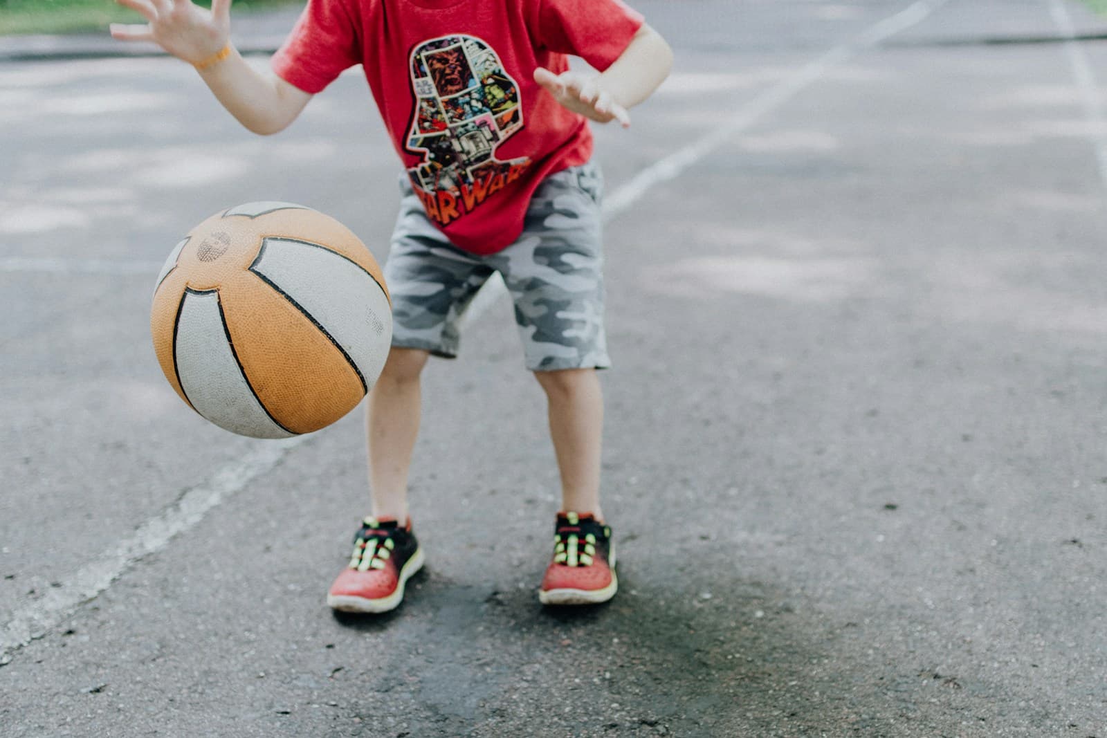 A young child in a T-shirt bouncing a basketball on an outdoor court